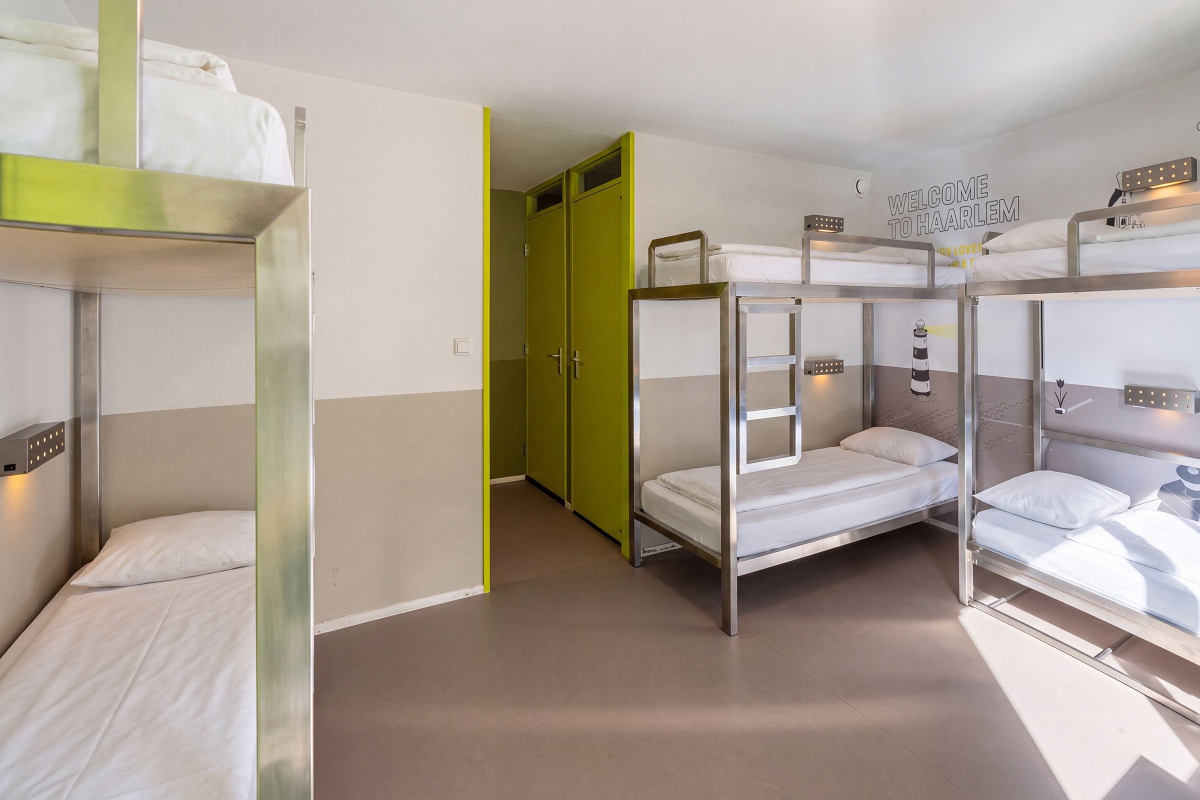 A dormitory room with bunk beds, a green door, and a welcome sign.