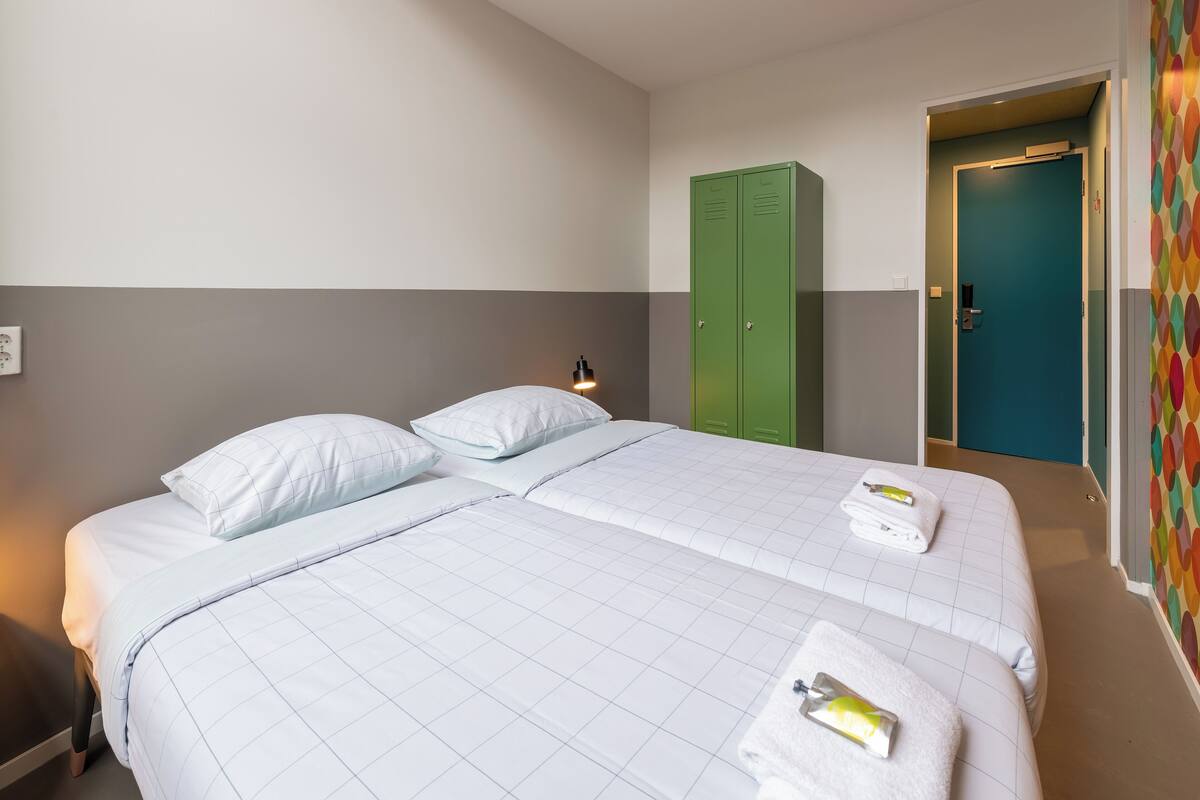 Una habitación de hotel con dos camas, un armario verde y una pared colorida.