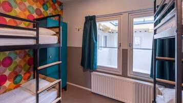 A dormitory room with bunk beds, a window with curtains, and a radiator.