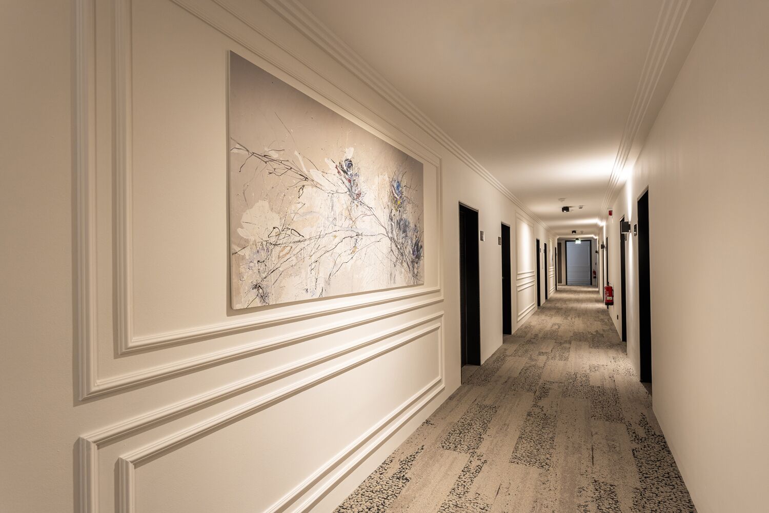 Un pasillo con un cuadro de pared de mármol, paneles blancos y una alfombra estampada.