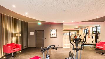 Ein modernes Fitnessstudio mit Trainingsgeräten, roten Sitzgelegenheiten und einem glanzverzierten Holzboden.
