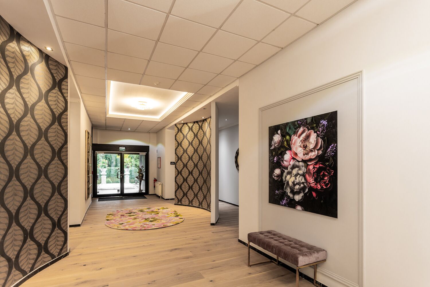 Een gang met behang, een houten vloer, een bankje en een bloemschilderij.
