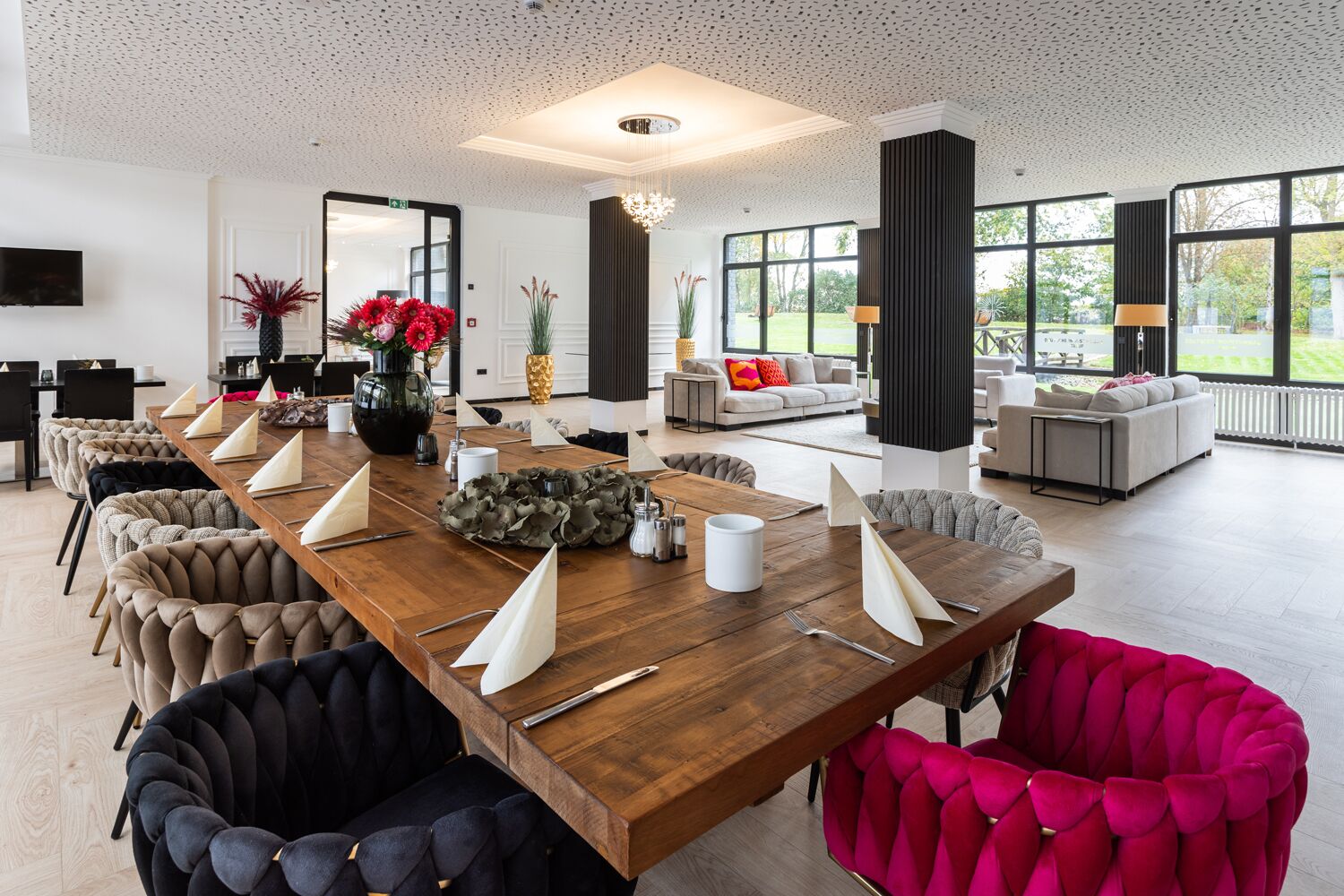 Un comedor amplio con una larga mesa de madera, sillas tapizadas y una lámpara de araña moderna.