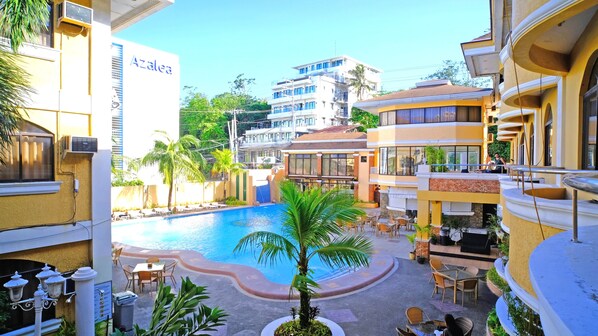 A hotel courtyard with a swimming pool, outdoor seating, and a view of surrounding buildings.