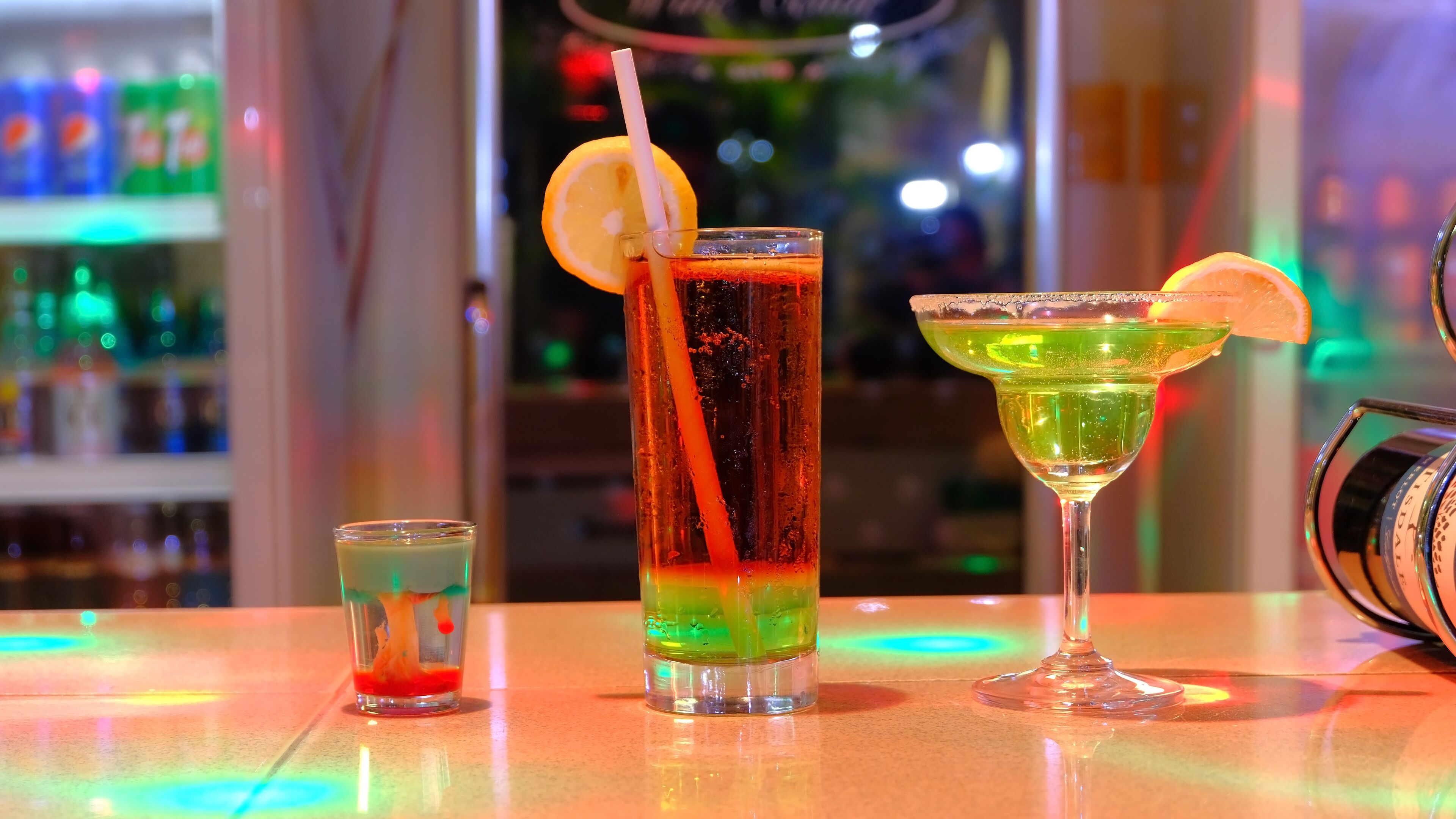 Three cocktails on a bar counter with a blurred background of shelves and bottles.