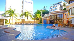 A hotel pool area with a clear view of the pool, lounge chairs, and a restaurant with outdoor seating.