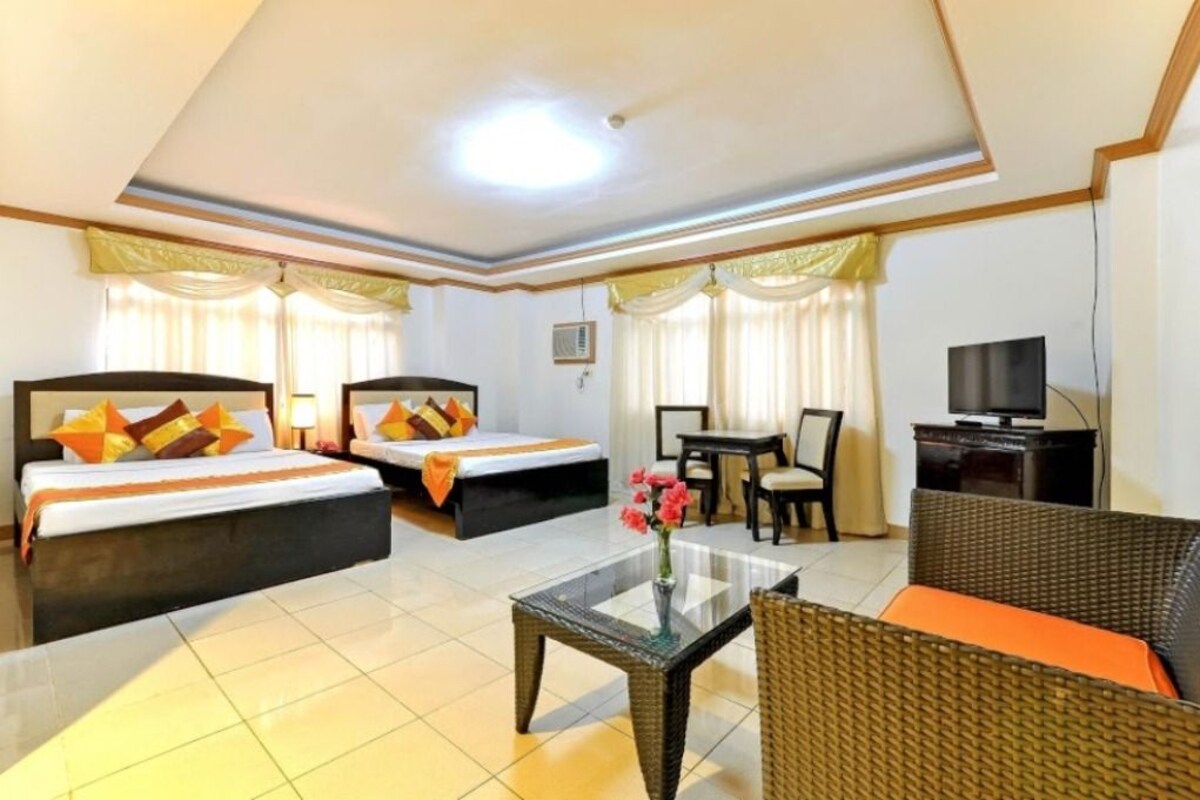 A hotel room with two beds, a television, a glass coffee table, and a wicker sofa.