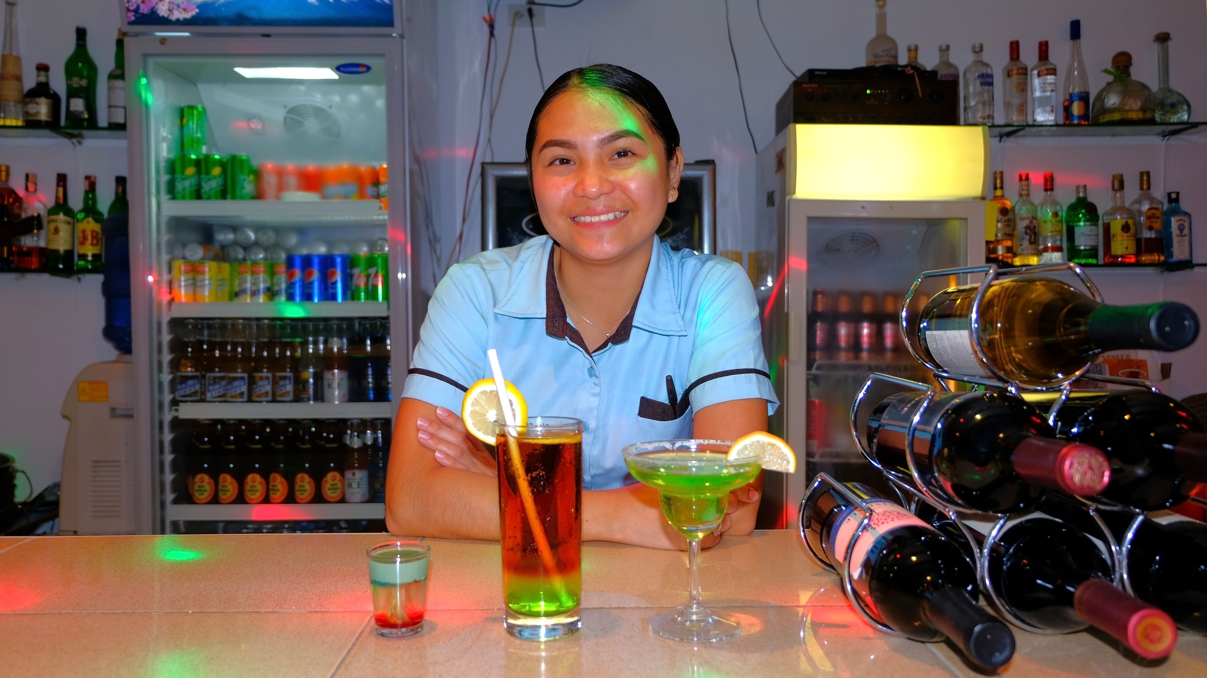 A bar area with a refrigerator stocked with beverages, a wine rack, and a person holding a drink.