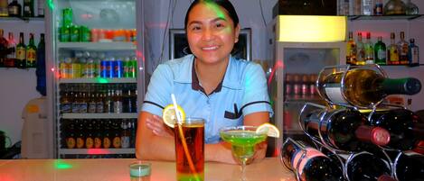 A bar area with a refrigerator stocked with beverages, a wine rack, and a person holding a drink.