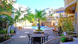 A poolside area with outdoor seating, a central palm tree, and a view of a building with balconies.