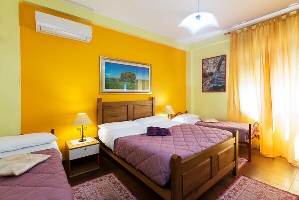A hotel room with two single beds, a wooden headboard, a nightstand with a lamp, a wall-mounted air conditioner, and two framed pictures. - Guest House Aio Sardegna (Cagliari)