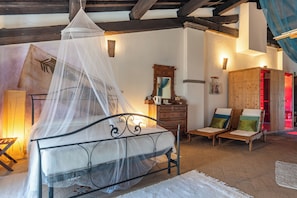 A room with a bed, a wooden cabinet, a mirror, and two lounge chairs.