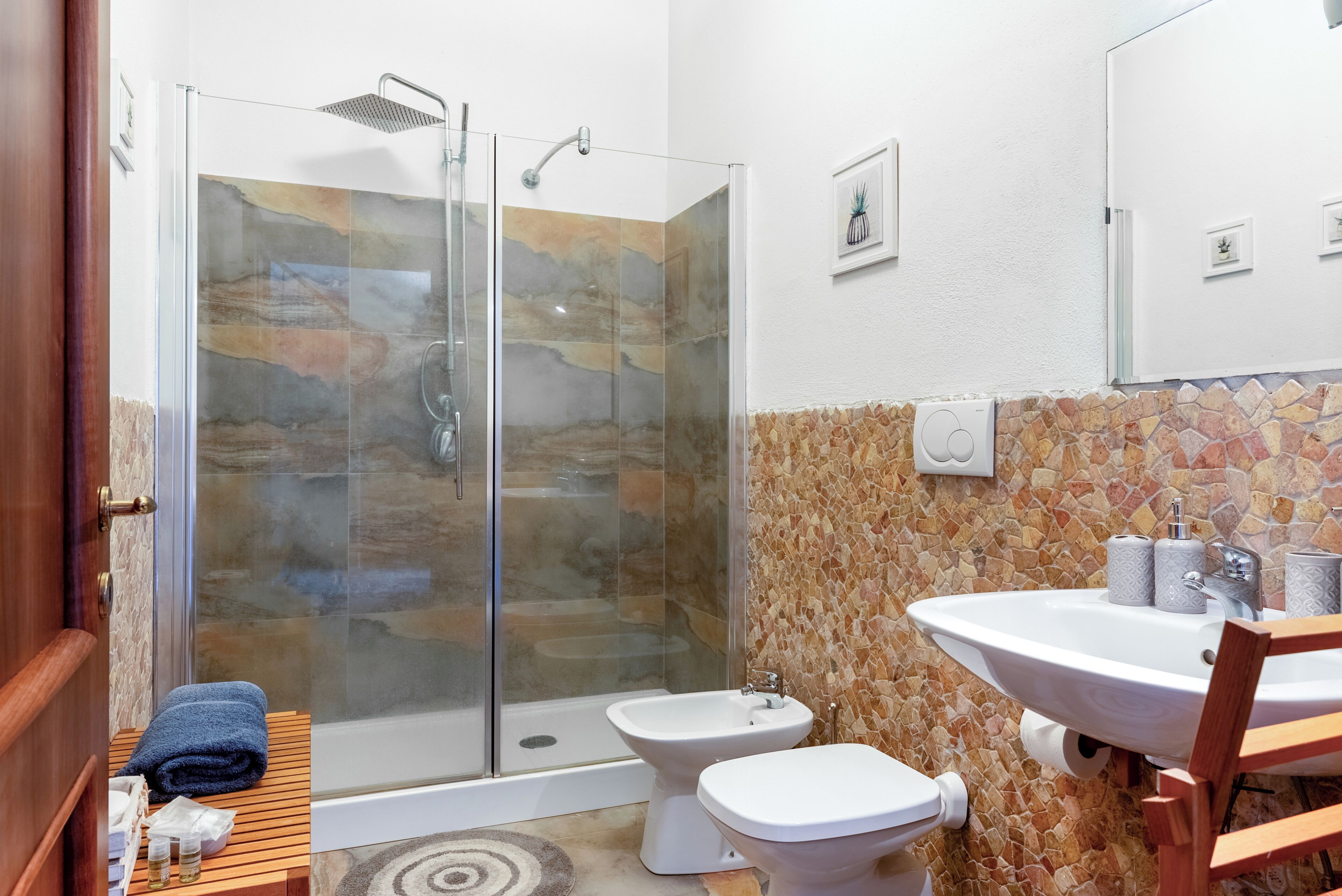 A bathroom with a glass-enclosed shower, a white sink, and two toilets.