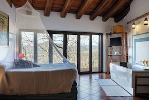 A bedroom with a bed, a TV, a wooden ceiling, and a view through a glass door.