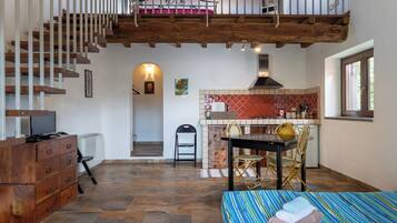 Une pièce spacieuse avec un escalier en bois, un coin repas avec une table et des chaises, une cuisine avec un plan de travail carrelé de carreaux rouges, et un lit avec une literie à rayures.