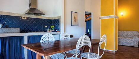 A dining area with a wooden table and white chairs, a kitchen with blue tiles, and a yellow wall.