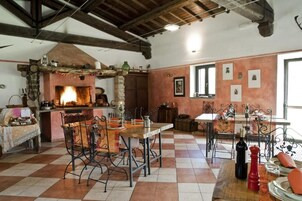 A rustic kitchen with a fireplace, a dining area with metal chairs, and a checkered floor.