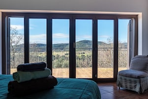 A room with a bed, a chair, and a view of a balcony with a railing.