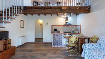 Ein geräumiges Zimmer mit einer Holztreppe, einem Essbereich mit Stühlen, einer Couch und einer Küchenzeile mit Arbeitsfläche und Sitzgelegenheiten.