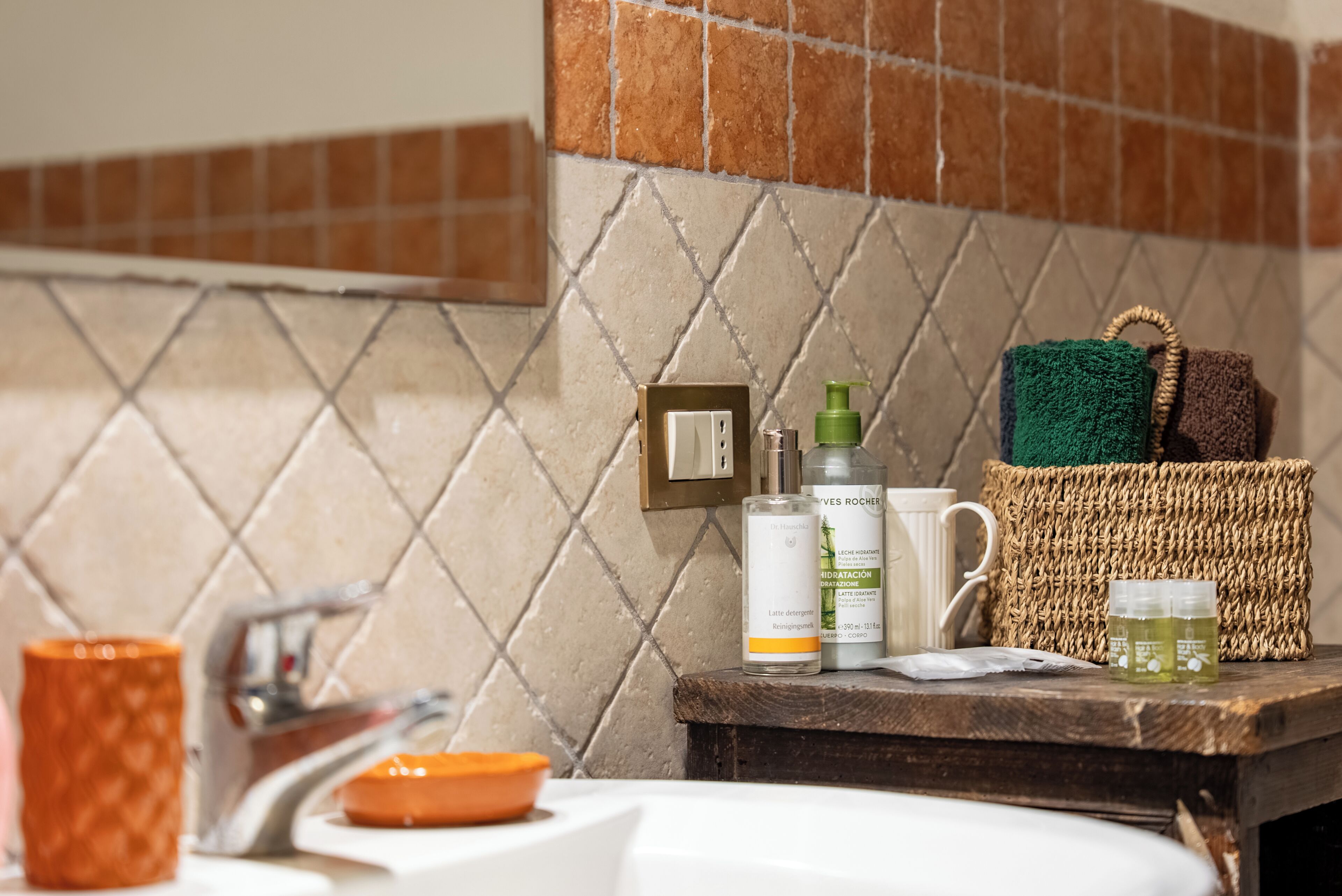 Un baño con salpicadero de azulejos, un lavabo, un espejo y artículos de aseo en la encimera.