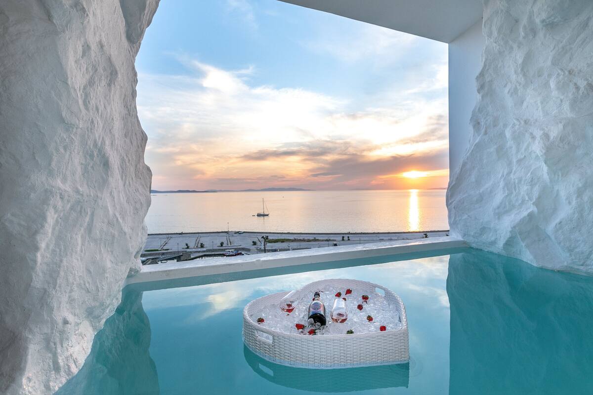 Una piscina de hielo lujosa con una silla de mimbre y pétalos de rosa, con vistas a la puesta de sol sobre el mar.