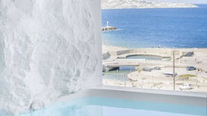 Vista desde una habitación con pared blanca y ventana que da a una zona costera con piscina y muelle.