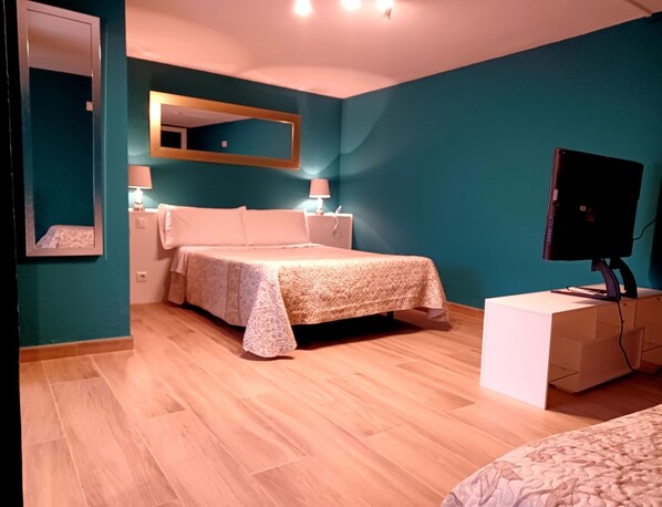Un dormitorio con cama, lámparas de noche, televisor y espejo en paredes color turquesa.