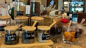 Diversos alimentos en frascos con etiquetas, como frutas secas y semillas, sobre una encimera.
