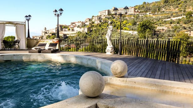 Zona de piscina con cubierta de madera, balaustradas de piedra y una estatua.
