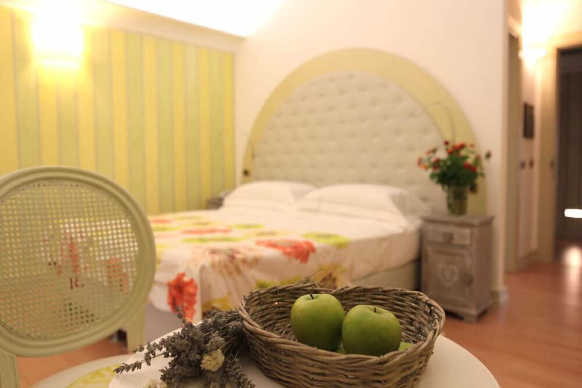 Ein Schlafzimmer mit einem Bett, einem Korbwagen mit Äpfeln, einem Sessel und einem Nachttisch mit einer Pflanze.