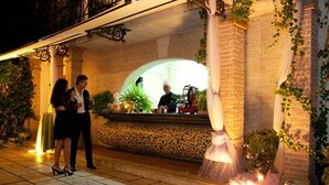 Un área de recepción al aire libre con un banco de piedra, una columna blanca y una fuente.