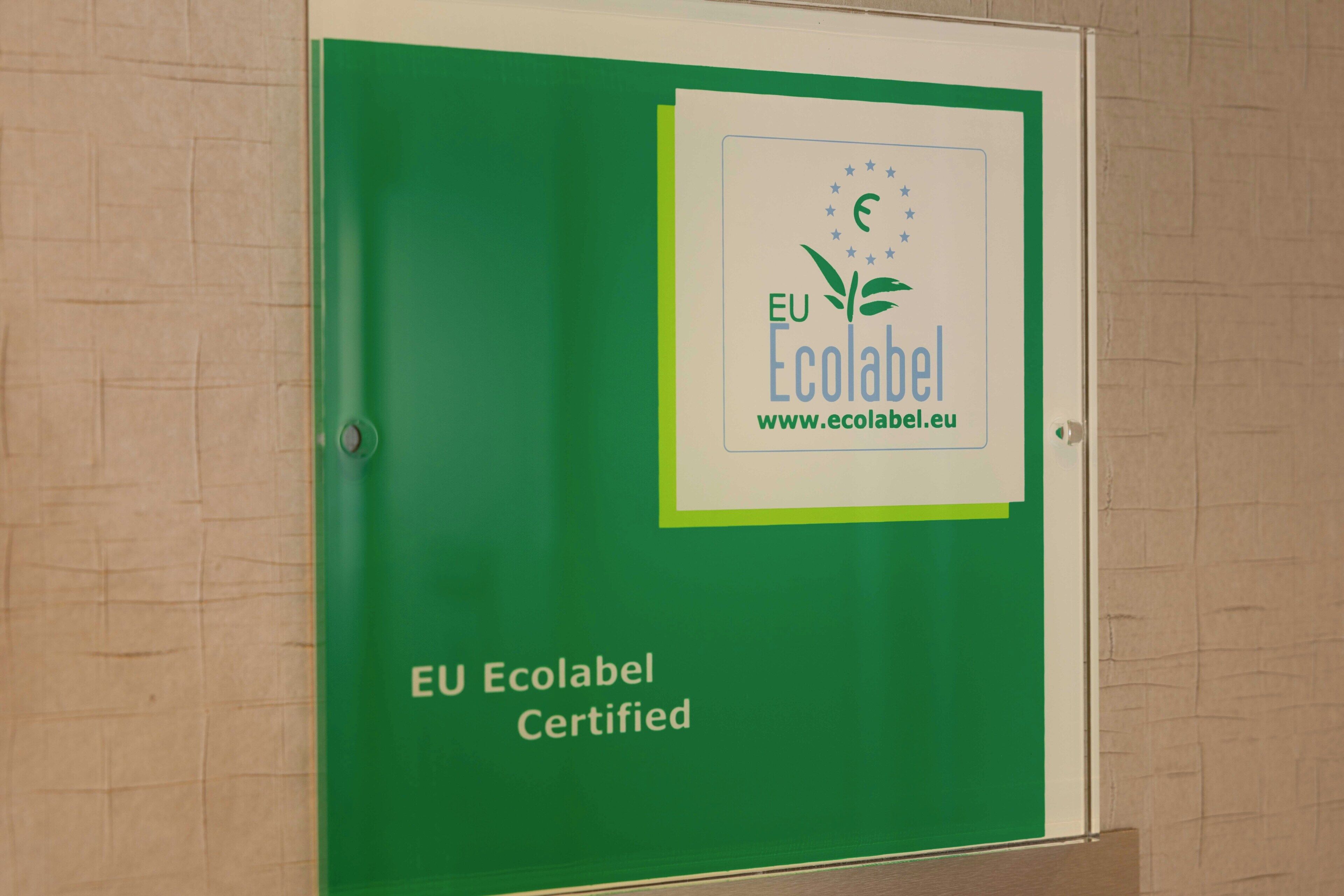 A green sign with the EU Ecolabel logo and the text 'EU Ecolabel Certified' on a wall.