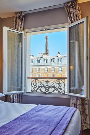 A room with a bed, a window with curtains, and a view of the Eiffel Tower. - Hôtel Le Relais Saint Charles (Paris)