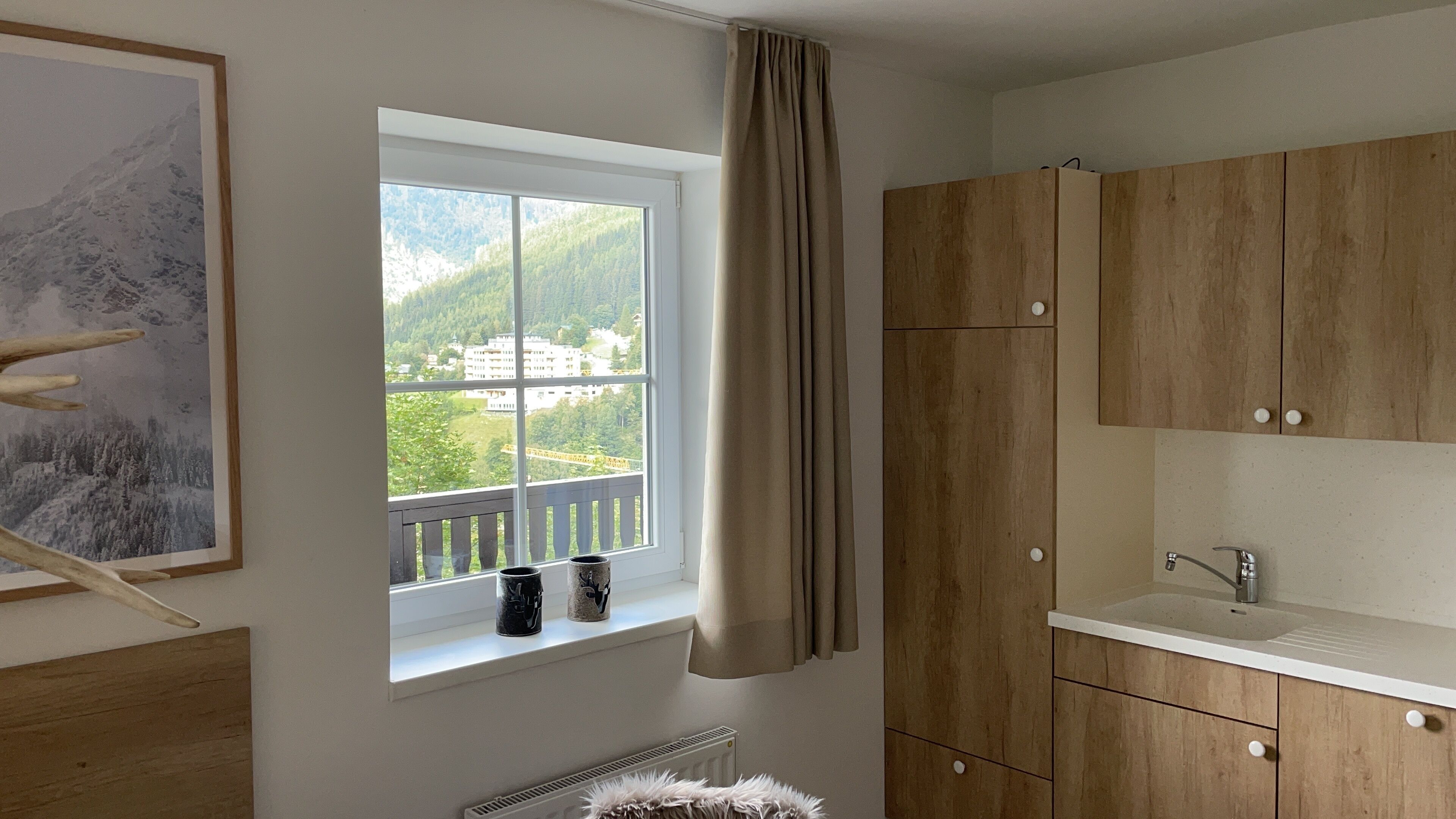 A modern kitchen with wooden cabinets, a white countertop, and a window with a view of a mountain and buildings.