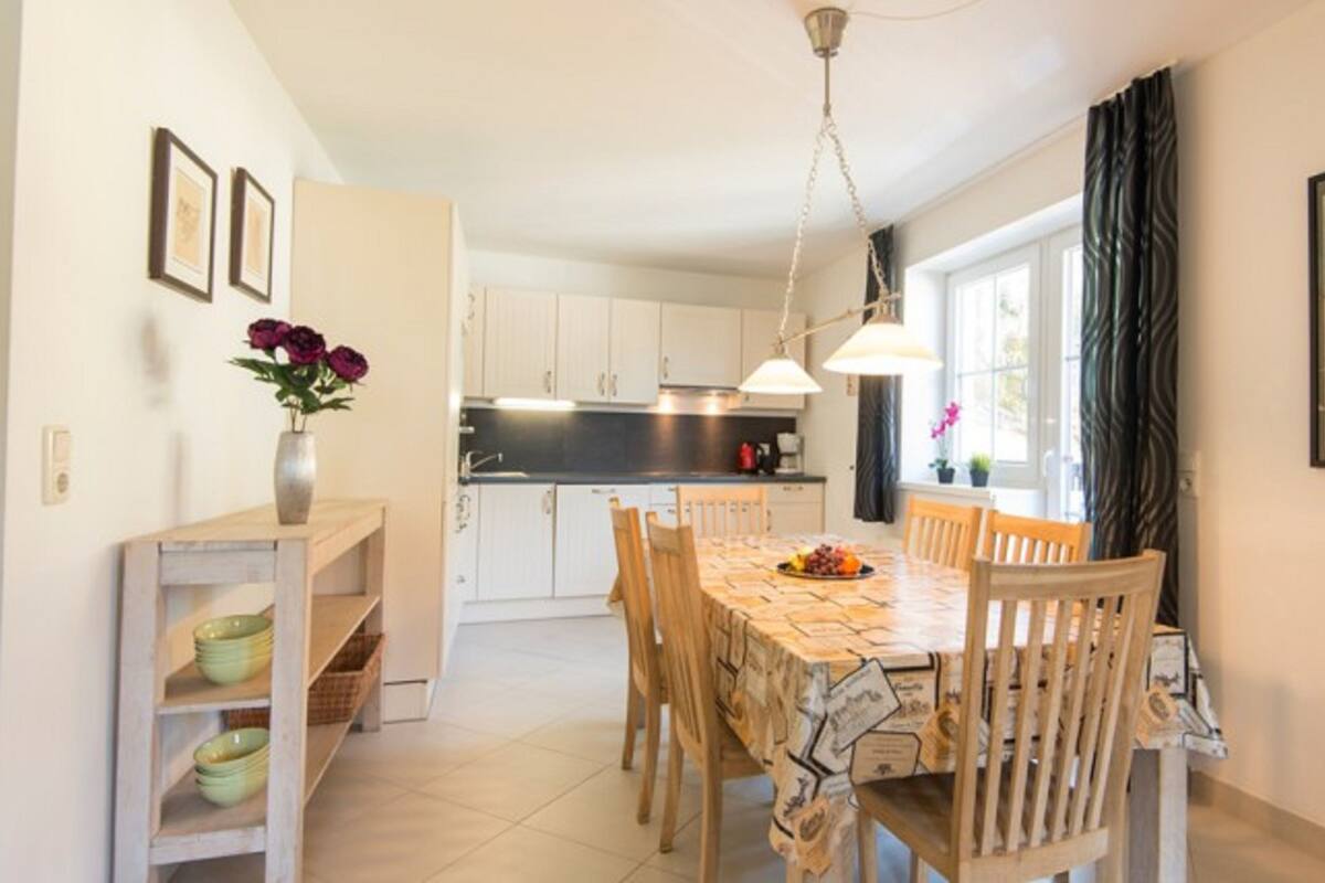 A modern kitchen with white cabinets, a dining table with chairs, and a vase with flowers on a shelf.