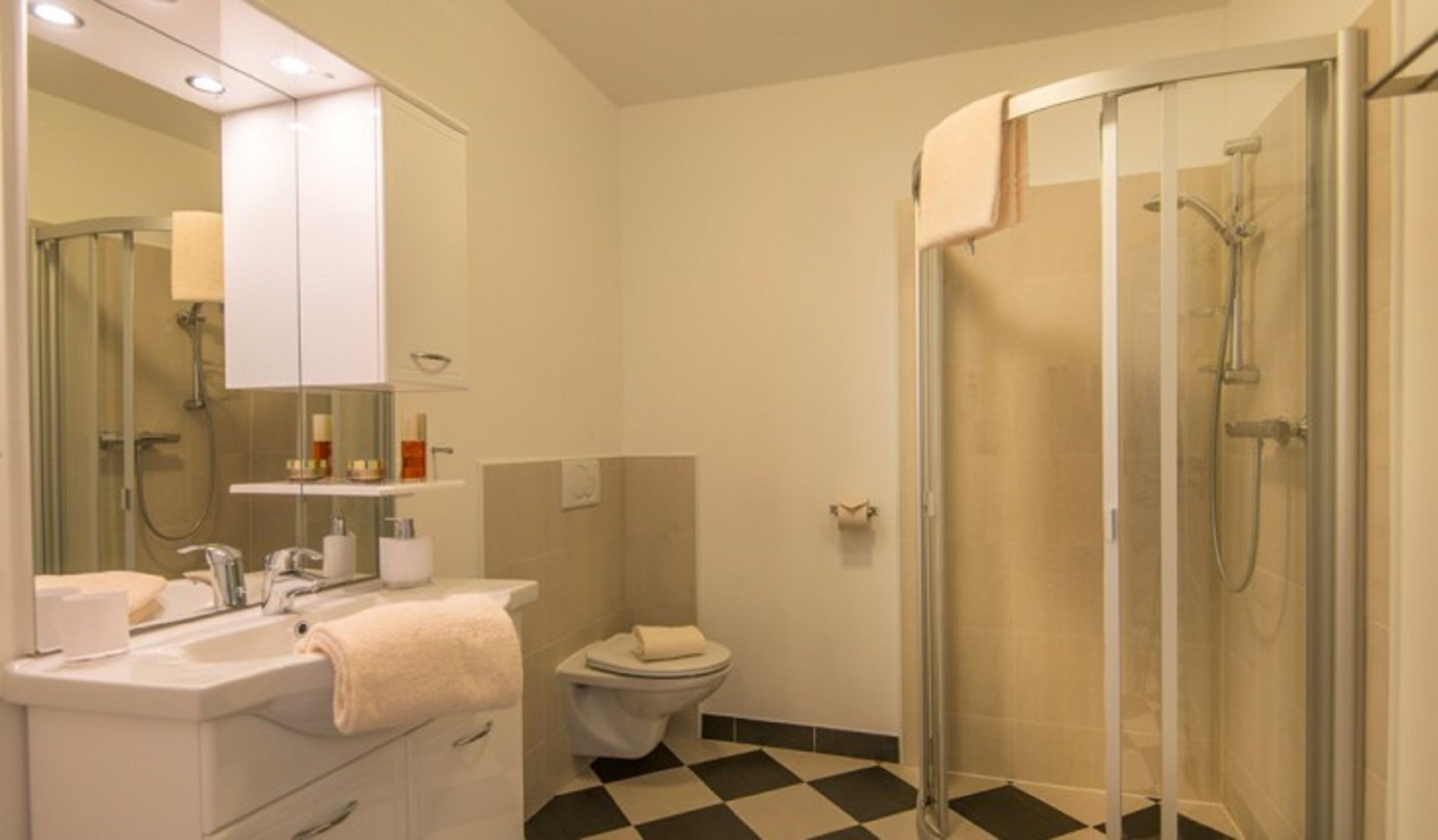 Un baño moderno con lavamanos, espejo, inodoro y ducha con mampara de vidrio.