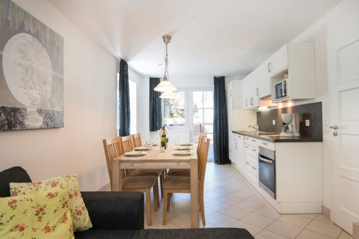 A modern kitchen with white cabinets, a dining area with a wooden table and chairs, and a large painting on the wall.