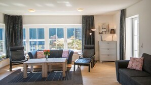 A modern living room with a sofa set, a coffee table, and a dining table. There is a view of the outdoors through large windows. - Alpenhof (Bad Gastein)