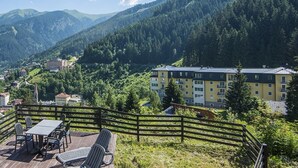 A balcony with a table and chairs overlooking a mountainous village with buildings and greenery. - Alpenhof (Bad Gastein)