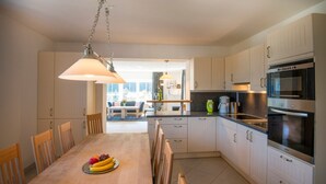 A modern kitchen with white cabinets, a dining table with chairs, and a large oven. - Alpenhof (Bad Gastein)