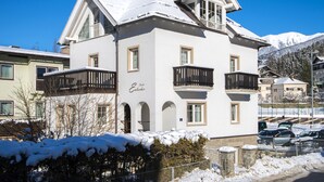 Un hotel su due piani con balconi, un tetto innevato e montagne sullo sfondo.