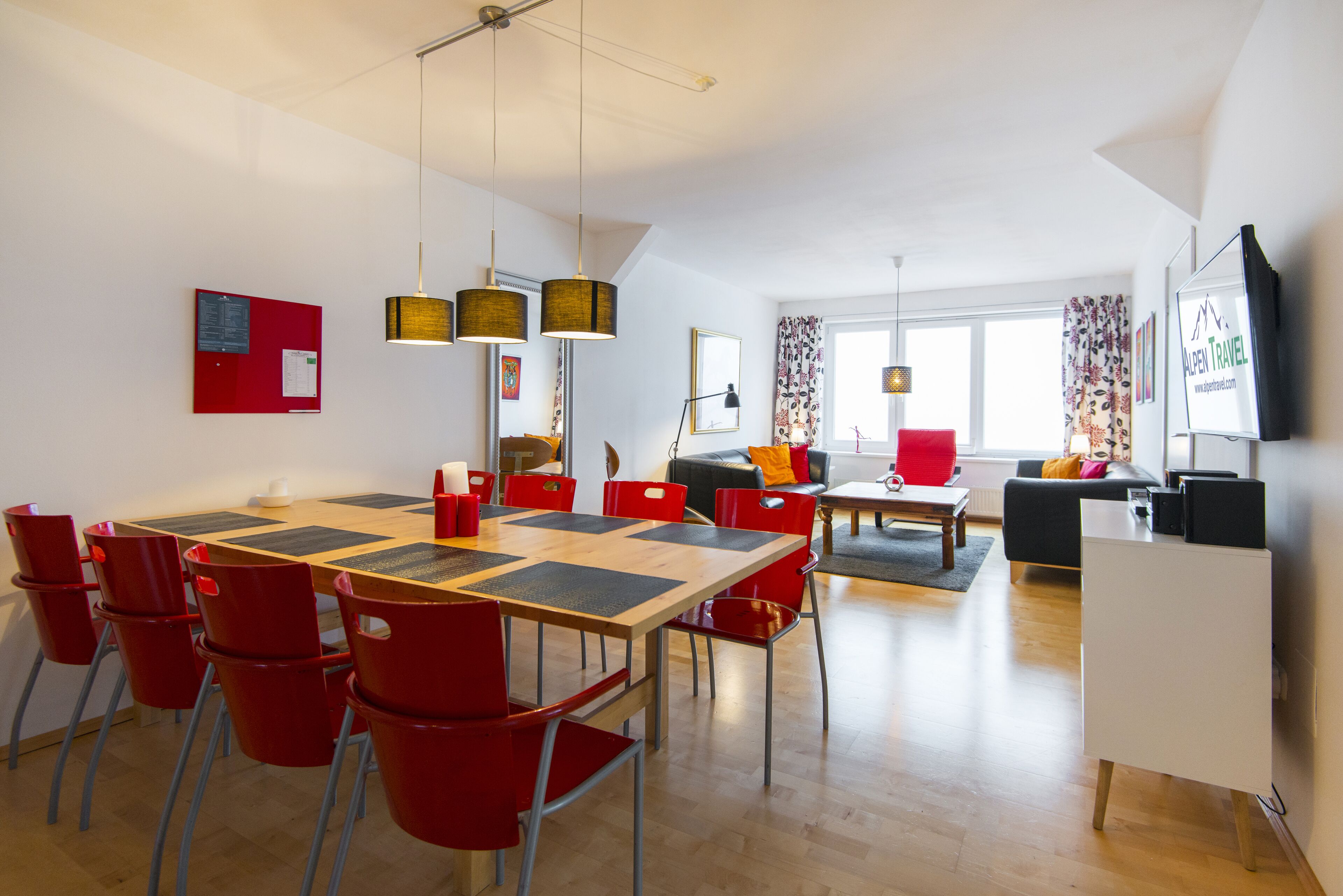 Un salon moderne avec un coin repas, comprenant une table à manger en bois, des chaises rouges, un canapé et un téléviseur.