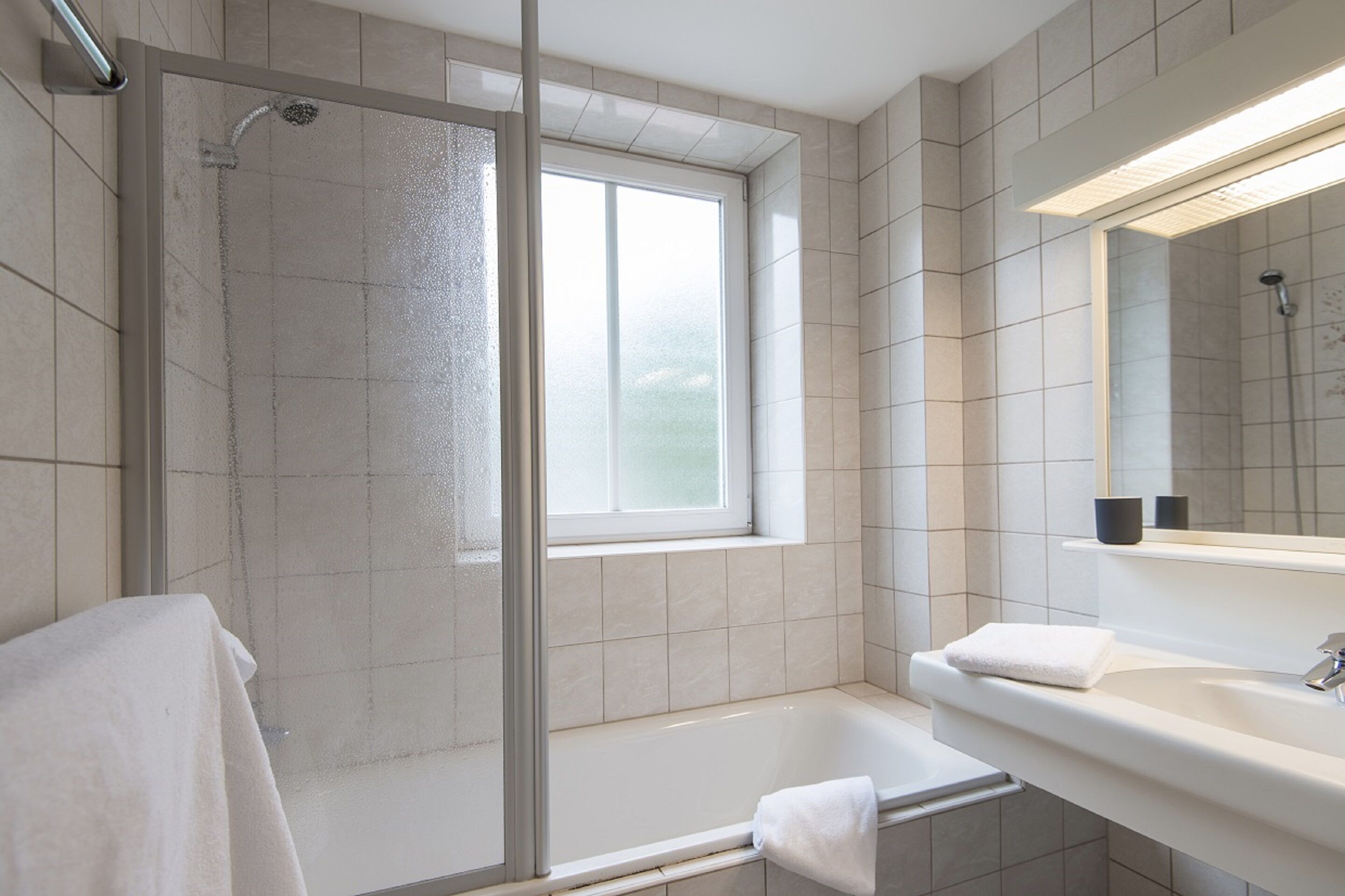 A modern bathroom with a glass-enclosed shower, a bathtub, a sink with a mirror, and a window providing natural light.