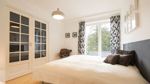 Un dormitorio con una cama grande, un armario con puertas de cristal, una silla y una ventana con cortinas.