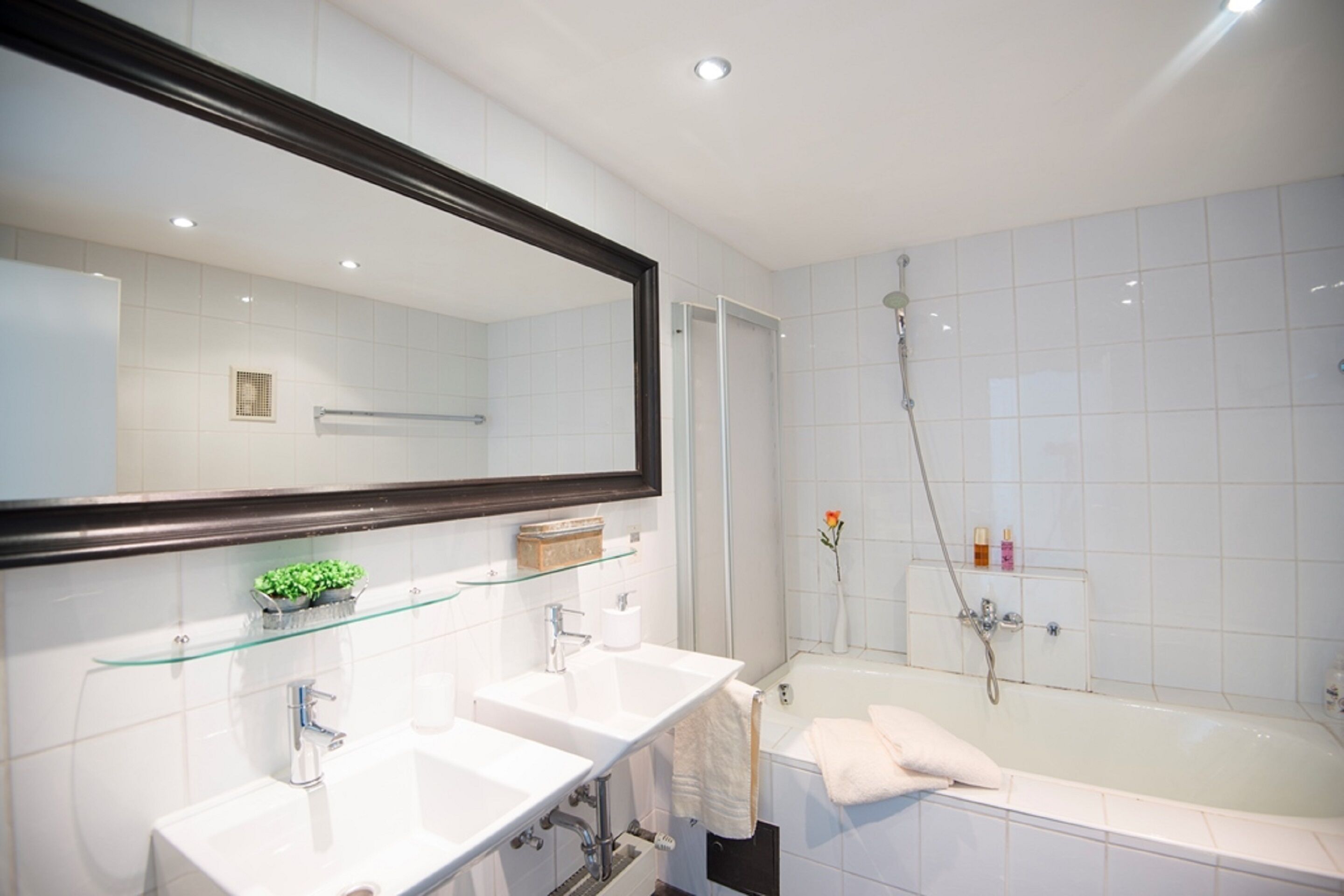 A modern bathroom with two sinks, a large mirror, a bathtub, and a shower.