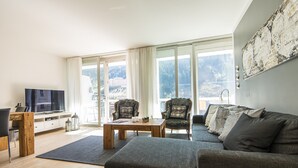 A modern living room with a large window, a flat-screen TV, a wooden coffee table, and a grey sofa. - Haus Lothringen (Bad Gastein)