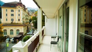 A balcony with a table and chairs, overlooking a street with parked cars and buildings. - Haus Lothringen (Bad Gastein)