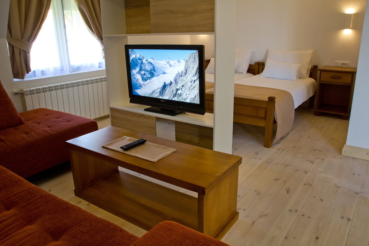 A hotel room with a bed, a TV on a wooden stand, a wooden coffee table, and a red sofa.