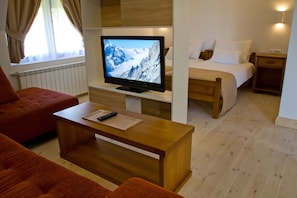 A hotel room with a bed, a TV on a wooden stand, a wooden coffee table, and a red sofa.
