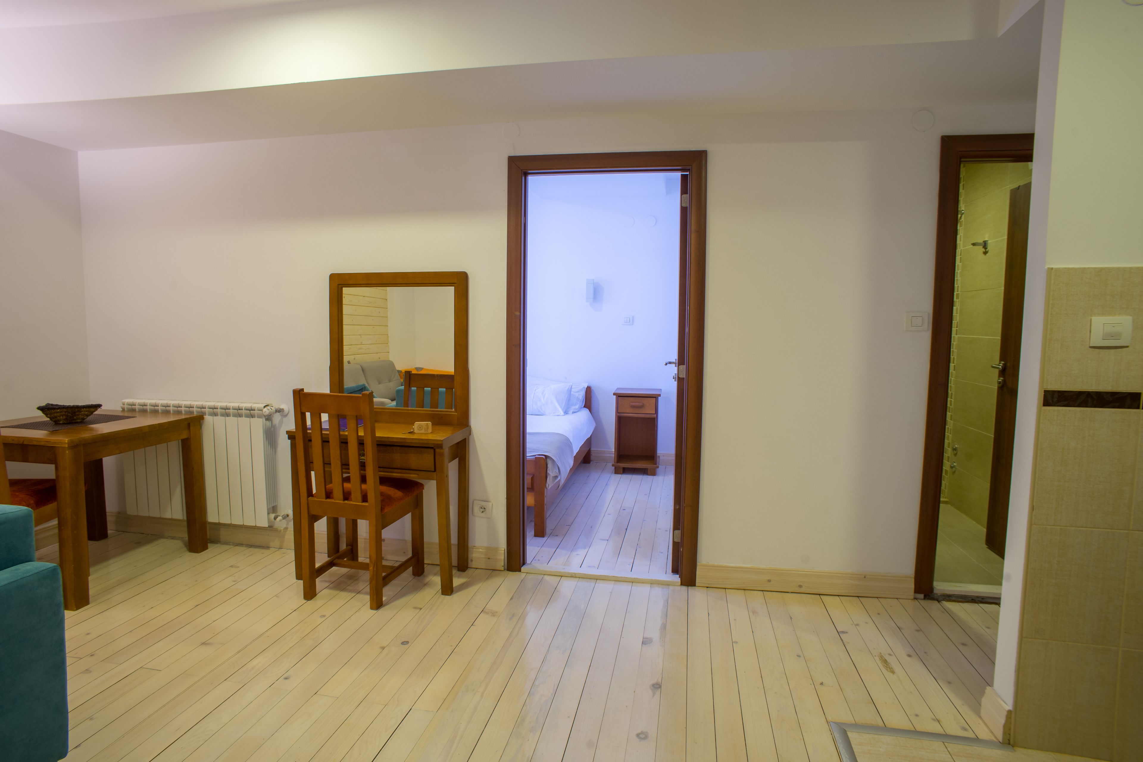 Una habitación con piso de madera, una cama, una mesita con una silla, un espejo y un radiador.